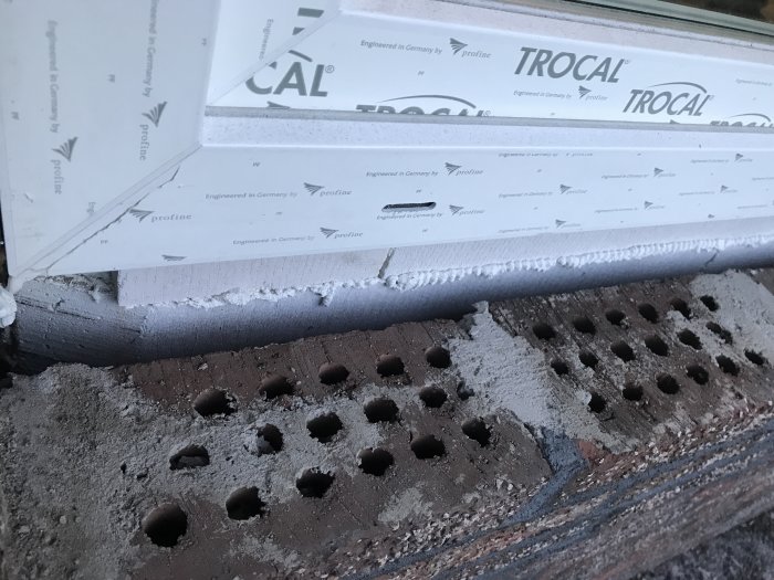 Närbild på en delvis isolerad vägg vid fönsterinstallation med synligt tegel och skum.