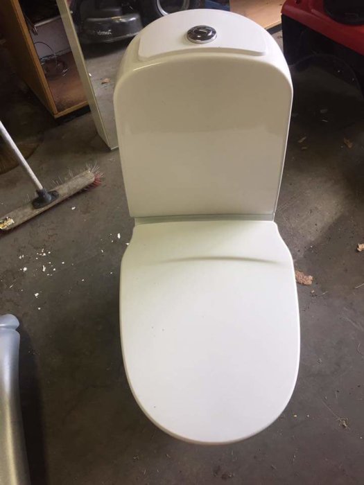 Begagnad vit toastol med stängt lock och dubbelspolningsknapp i ett garage.