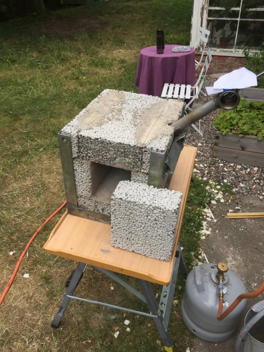 Hembyggd ässja för metallarbete med gasoltub, placerad på en arbetsbock utomhus.