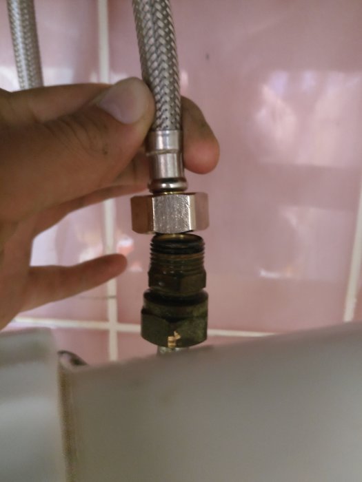 Hand som håller en stålomspunnen slangs ände mot ett badrumsrör som behöver en adapter eller förlängare.