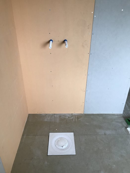 Utomslutet badrum under renovering med synlig golvbrunn och rörutgångar för duschblandare.