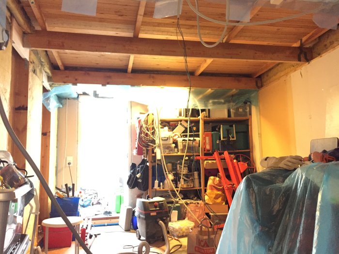 Ny upphängning på takbalkar i ett rum under renovering med rörigt byggmaterial och verktyg.