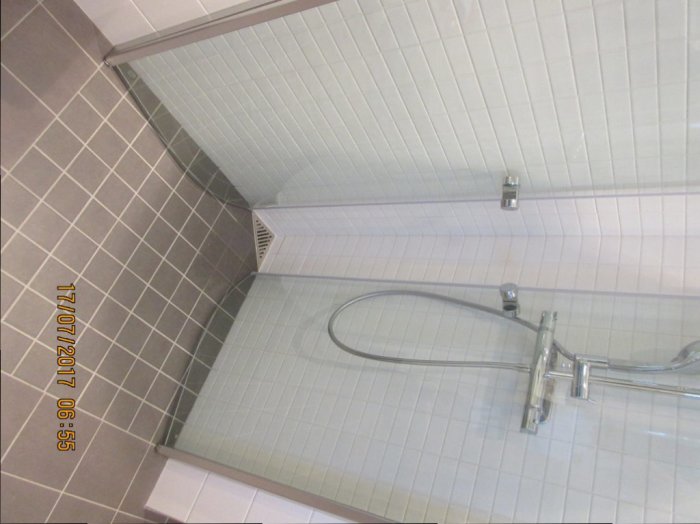 Nyrenoverad dusch med vita kakelväggar och grå klinkergolv.
