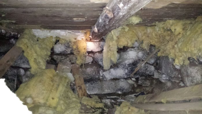 Förfallna isoleringsmaterial och träbjälkar med synlig mögeltillväxt i takkonstruktion, indikerar vattenskador och försummelse.