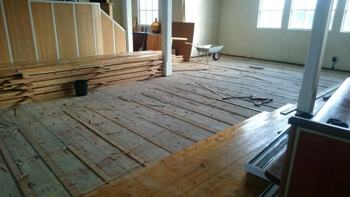 Renoveringsprojekt med upprivet trägolv, verktyg och trädgårdsskottkärra i tomt rum.