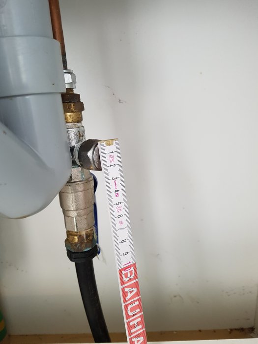 Mätning av vattenrörsanslutning under diskbänk med tumstock, T-koppling synlig.