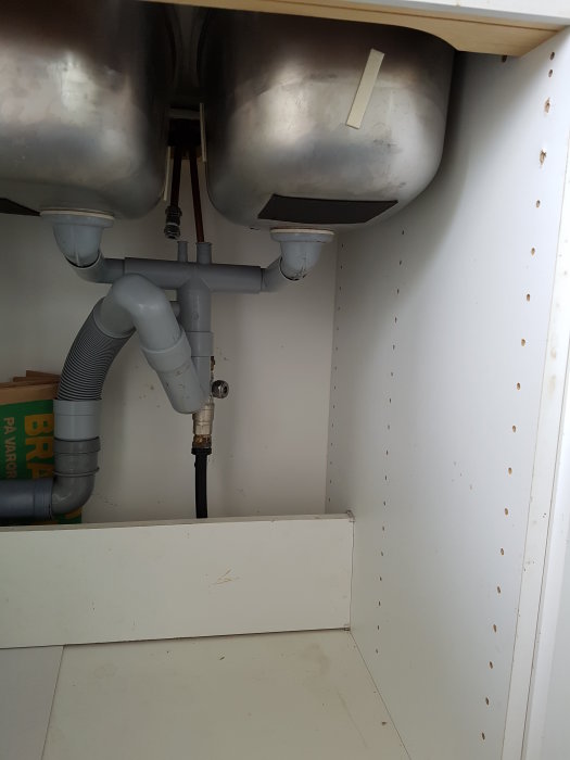 Undersida av diskbänk med synliga rör och T-koppling för kallvattenanslutning under renovering.