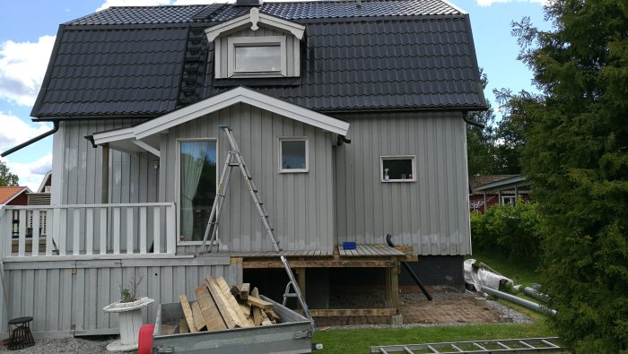 Ny målning på husets fasad och altan, stege lutad mot huset, byggmaterial på marken.