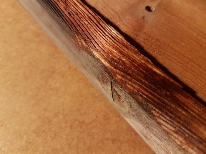 Närbild på nedre delen av ett gammalt träfönster med synliga sprickor och skador från fukt och solljus.