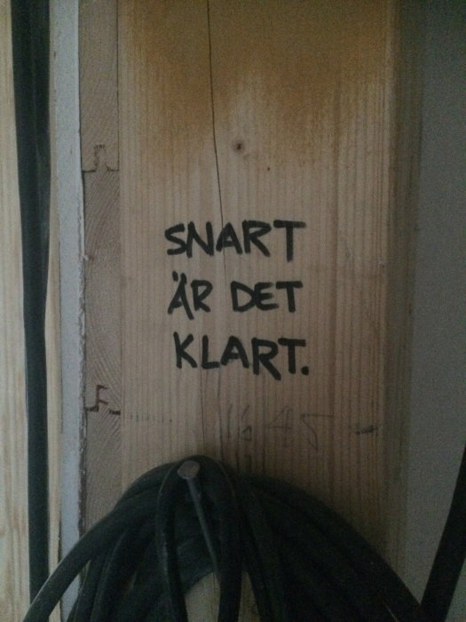 Trähölje med texten "SNART ÄR DET KLART" och en kabelrulle i ett under-renovering rum.