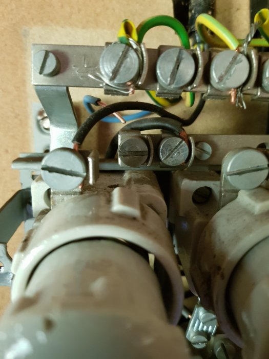 Närbild av en gammal undercentral med en lös nollkabel och tom skruvplats, intill säkringsklämmor.