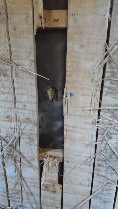 Rivna träbrädor avtäcker ett brunt pappersliknande skikt i en vägg från 1930-talet.