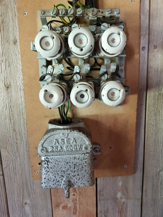 Gammal elektrisk central med flera keramiska säkringar och en metallhandske monterad på en trävägg.