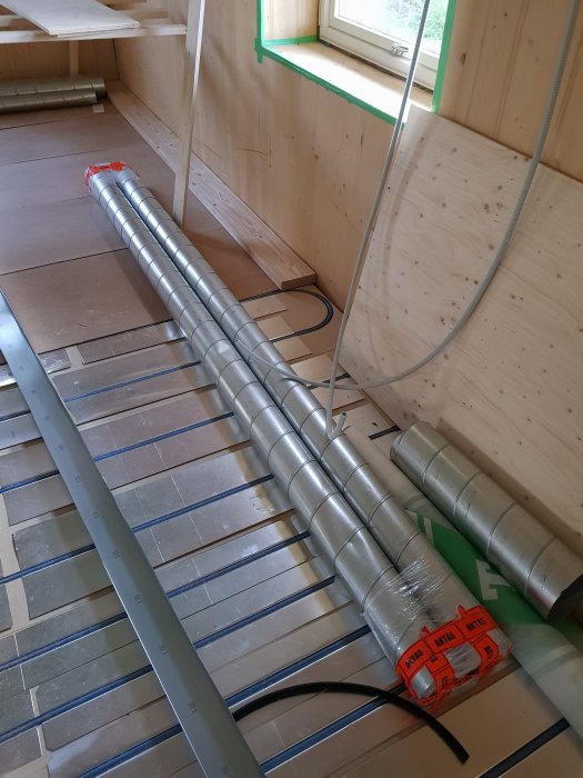 Spiro ventilation-rör och isoleringsmaterial på golvet i ett pågående byggprojekt.