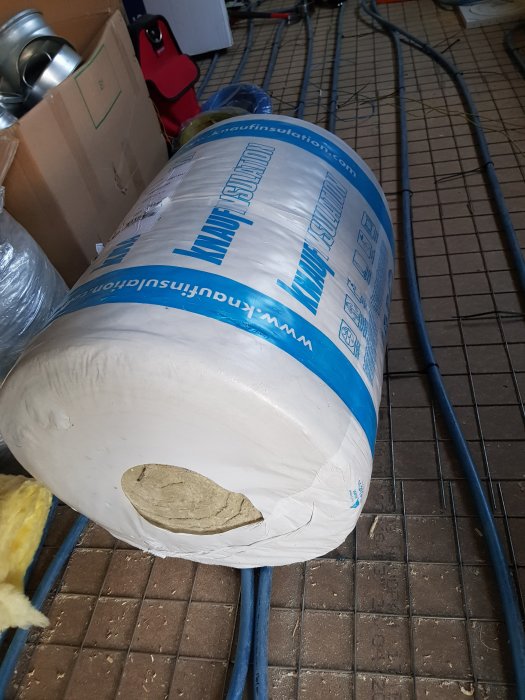 Rullad isoleringsmatta liggandes på ett tegelgolv med ventilationsrör i bakgrunden.