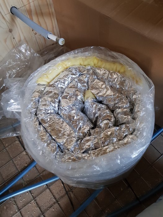 Isolerad nätmatta för imkanal insvept i plast, placerad på en vagn, med synlig gul isolering vid kanten.