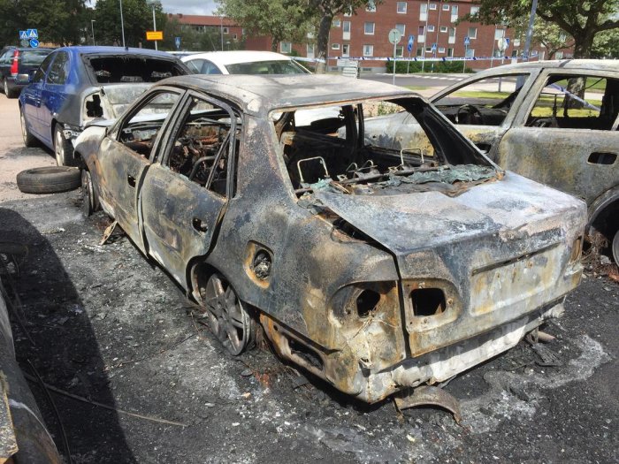 Utbränd bilskrov på en parkering visar omfattande brandskador och total förstörelse.