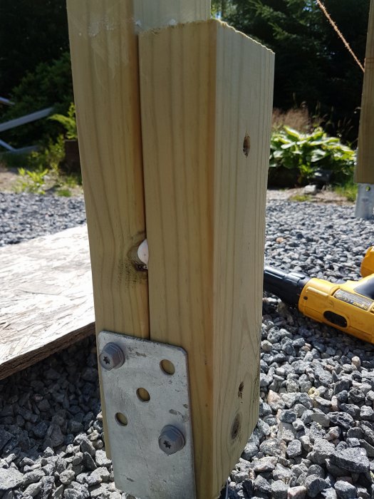 Sammansatta trästolpar limmade med PU-lim och förstärkta med en stolpsko samt skruvar, med en borr i bakgrunden.