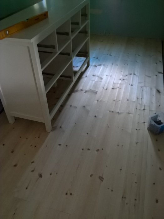 Ouppsatt hylla och vattenpass på ett nylagt trägolv med spikar och skräp efter renovering.