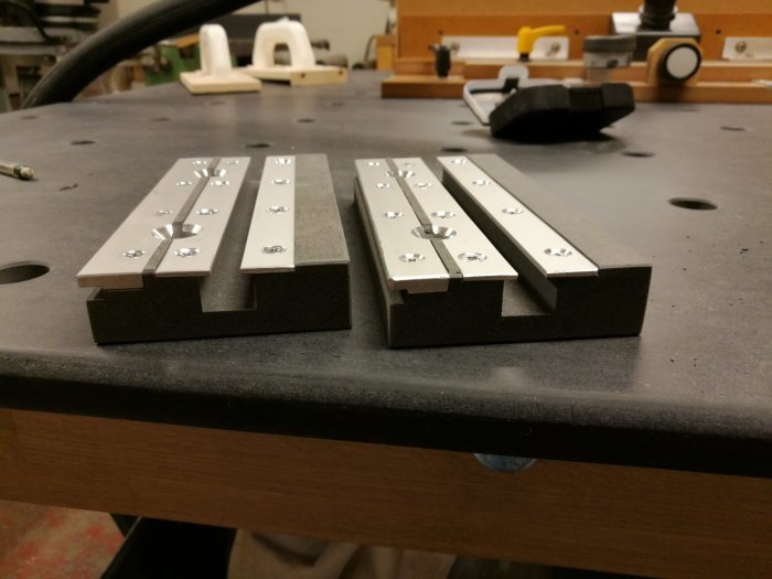 Aluminiumlister med frästa spår för vagnsbultar på ett verkstadsbord, med bakgrunden av en verkstad.