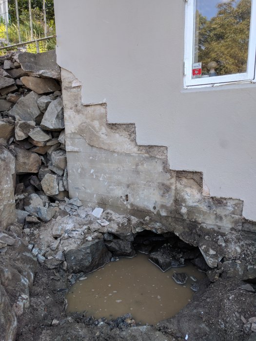 Riven trappa vid husvägg med en synlig vattenansamling under grunden i en byggnadsrenovering.