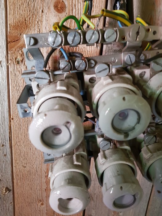 Gammal elinstallation med säkringshållare och kablar i ett uthus.