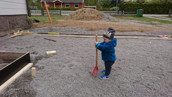 Barn hjälper till på byggplats med spade, grushög och konstruktionmaterial i bakgrunden.