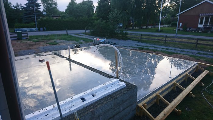 Färsk betongyta med reflektion av himlen omgiven av formar av trä och lecablock i ett byggprojekt.