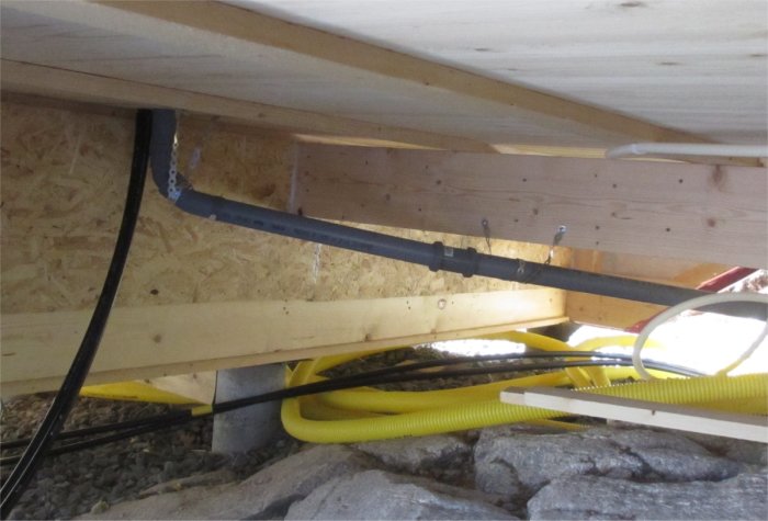 Diskavloppsrör under ett Attefallshus med en svart PVC-slang som går mot en bostadsgrund på berggrund.