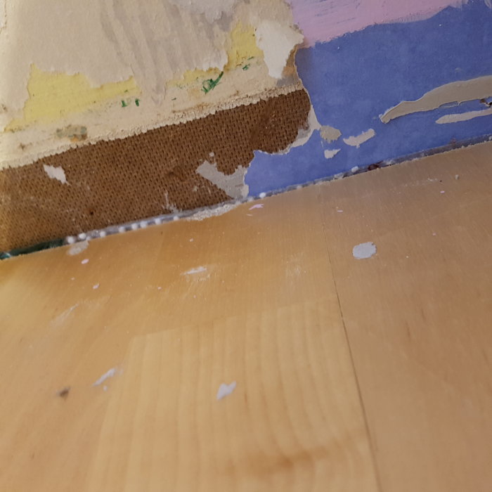 Delvis avlägsnad vägg med en synlig brun och gul materialskikt, eventuell misstanke om asbest.