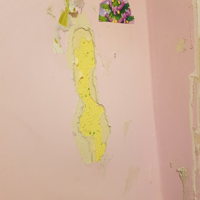 Vägg med rivet gips visar gul isolering, eventuellt asbest, bakom rosa målarfärg.