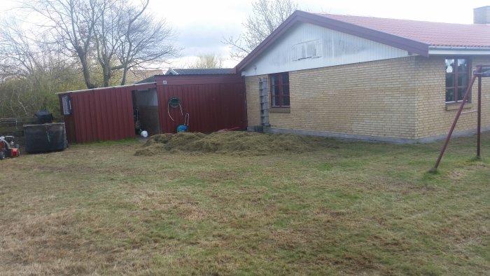 Trädgårdsprojekt med nyklippt gräsmatta, högar av gräsklipp och redskap vid en tegelvilla.