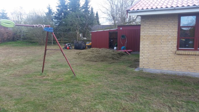 Trädgård under renovering med gräshögar, lekställning och diverse utomhusutrustning.
