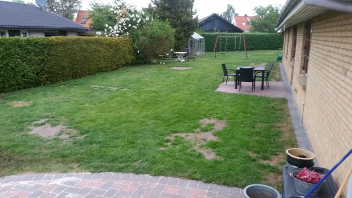 Trädgård med nyklippt gräsmatta, ojämna fläckar, utemöbler och lekställning i bakgrunden.
