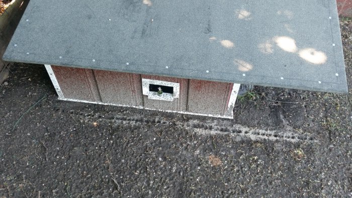 Ett hemmagjort skydd för robotgräsklippare med ett platt tak och en öppning på sidoväggen.