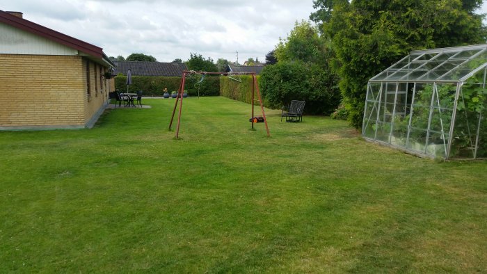 Välhållen gräsmatta med gungställning och växthus i en hemträdgård.