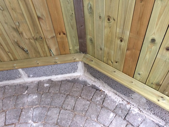 Träpanel möter stenläggning och en bräda vid en hörna, indikerar förberedelse för byggprojekt.
