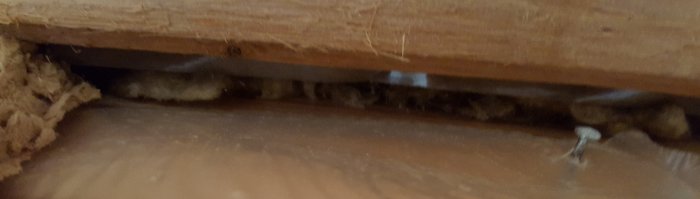 Utsnitt av en vägg där ångspärren inte når taket, exponerande isolering och ett mellanrum på cirka en centimeter.