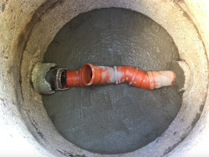 Glaserat keramikrör kopplat till brunn med betong, anpassning med markrör och värmepistol syns.