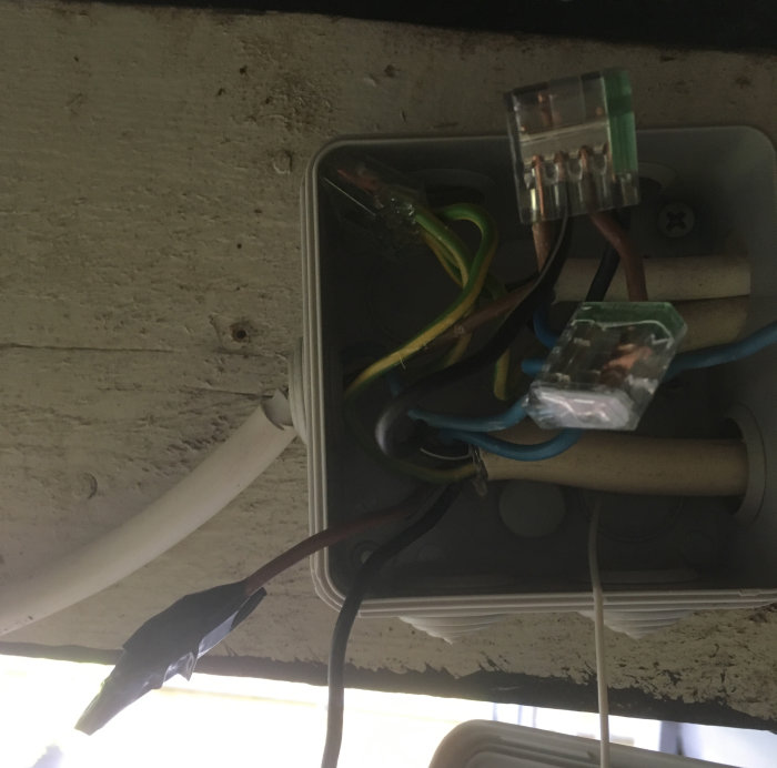 Elektriska ledningar och förbindningsklämmor i en öppen kopplingsdosa, sladd till vänster kopplad till lampa.