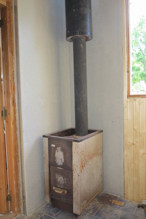 Rostig gammal kamin med skorsten inuti ett ofärdigt rum under renovering.