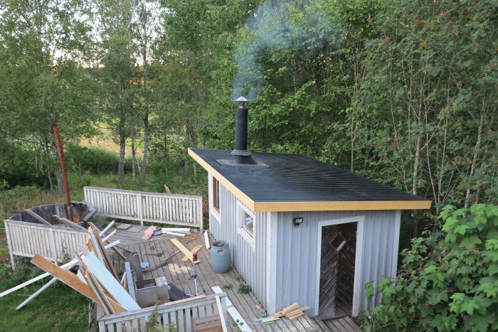 Ett nytt tak med skorsten och rök som väller ut bland byggavfall och grönska.