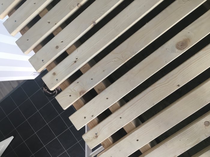 Installation av slang i glesregel på ett bygge, synlig mellan trälisterna mot en svart kaklad golvbakgrund.