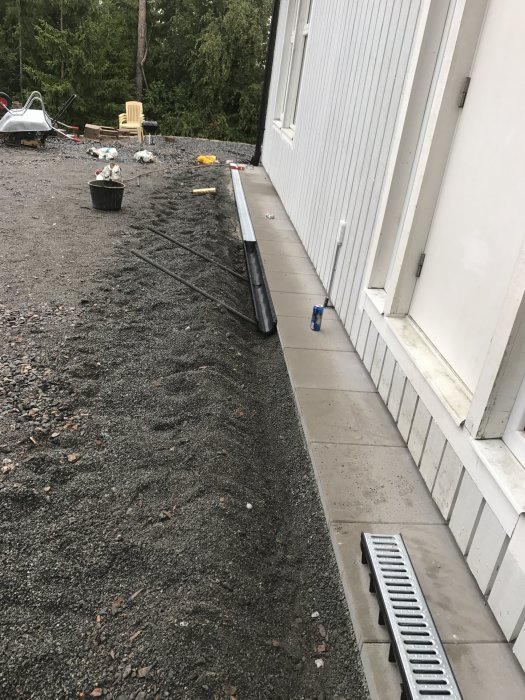 Nyinstallerad markränna längs husvägg med grus och byggmaterial i bakgrunden.
