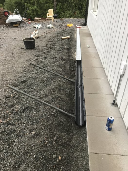 Installation av markränna längs grusbelagd uteplats under renovering med byggmaterial i bakgrunden.