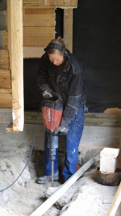 Person använder en bilmaskin för att gräva genom betonggolv inuti ett hus.