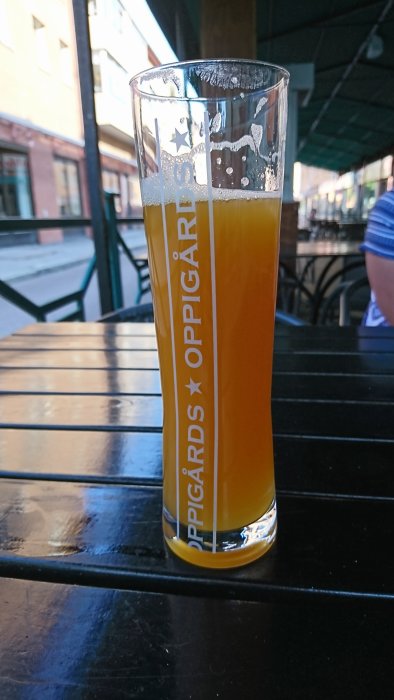 Ett glas med mango DIPA-öl på ett utomhusbord på en restaurang.