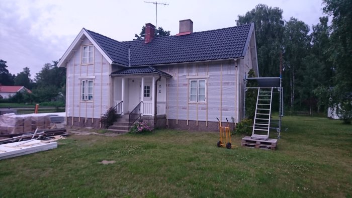 Hus under renovering med borttagen eternitbeklädnad och ny vindskyddsplast samt spikläkt installerad.