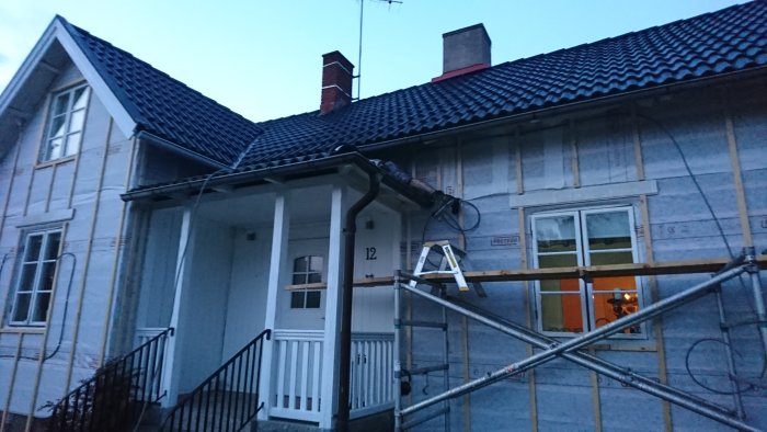 Renoveringsarbete på husfasaden med elinstallation för fasadbelysning vid skymning.