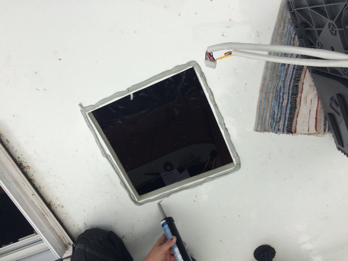 Utskuret fyrkantigt hål i husvagnstak med synlig isolering och kabel, tätmassa appliceras.